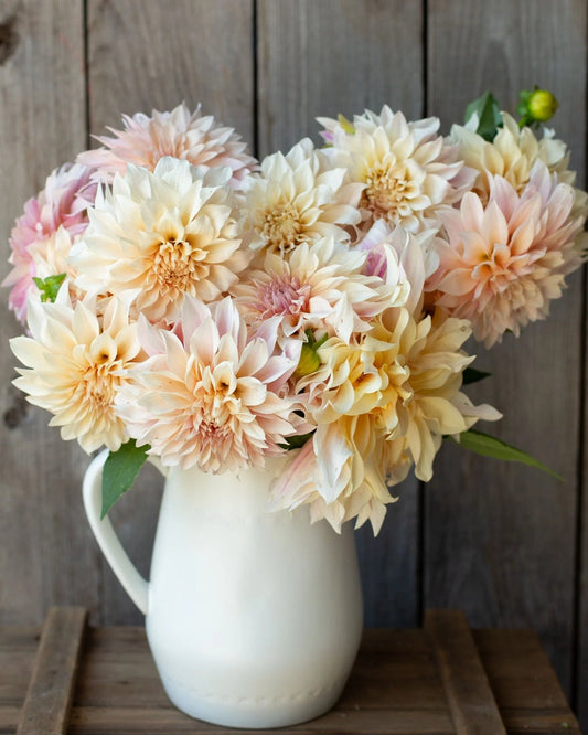 Bouquet of pastel-colored flowers in a white vase against a wooden background
